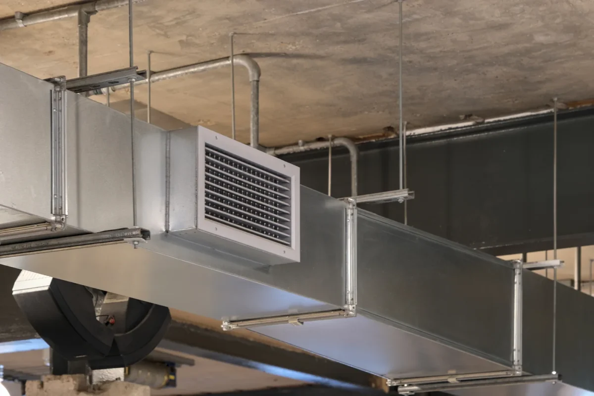 Metal ventilation ductwork and grilles suspended from an industrial ceiling