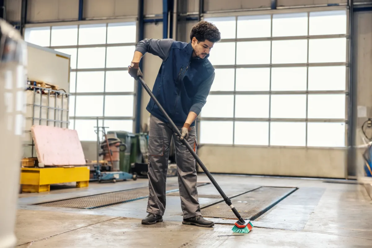 Worker sweeping the concrete floor around equipment in an industrial facility