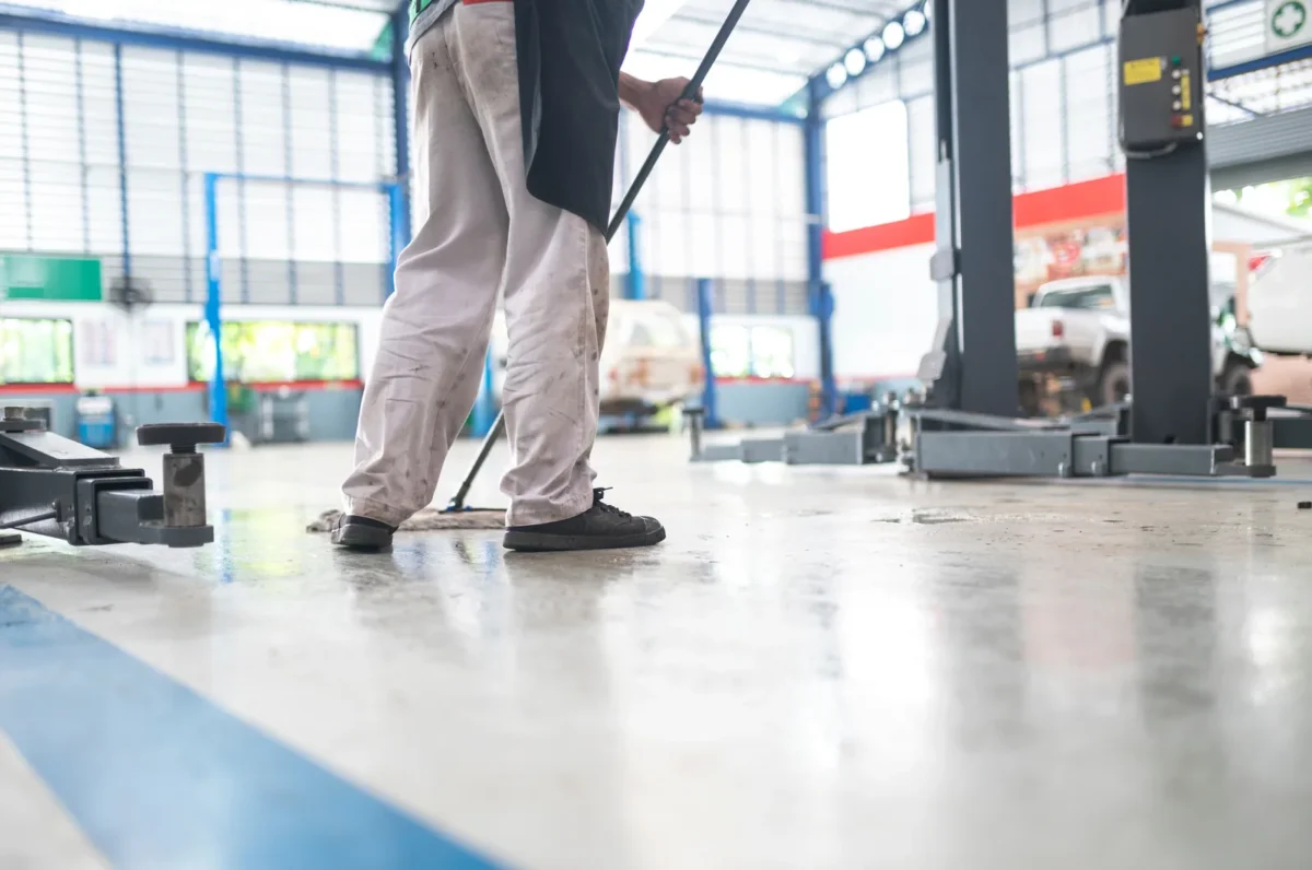 Worker using a floor squeegee in a vehicle repair workshop