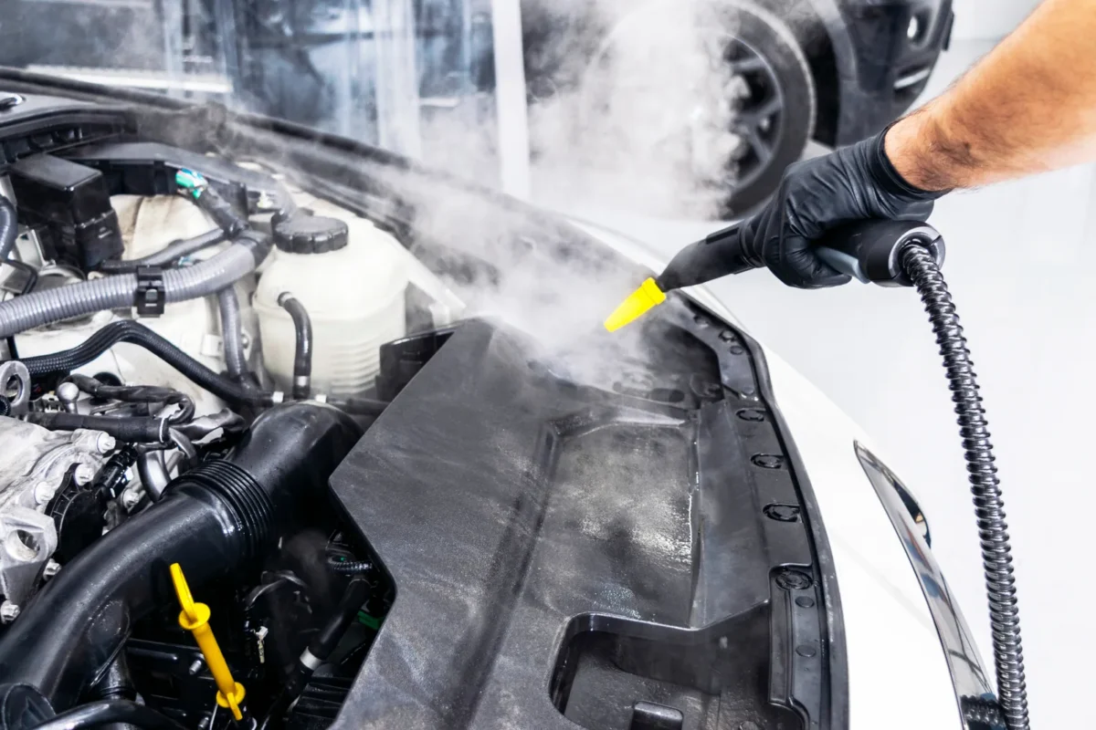 Steam-cleaning nozzle working around an engine bay in a workshop