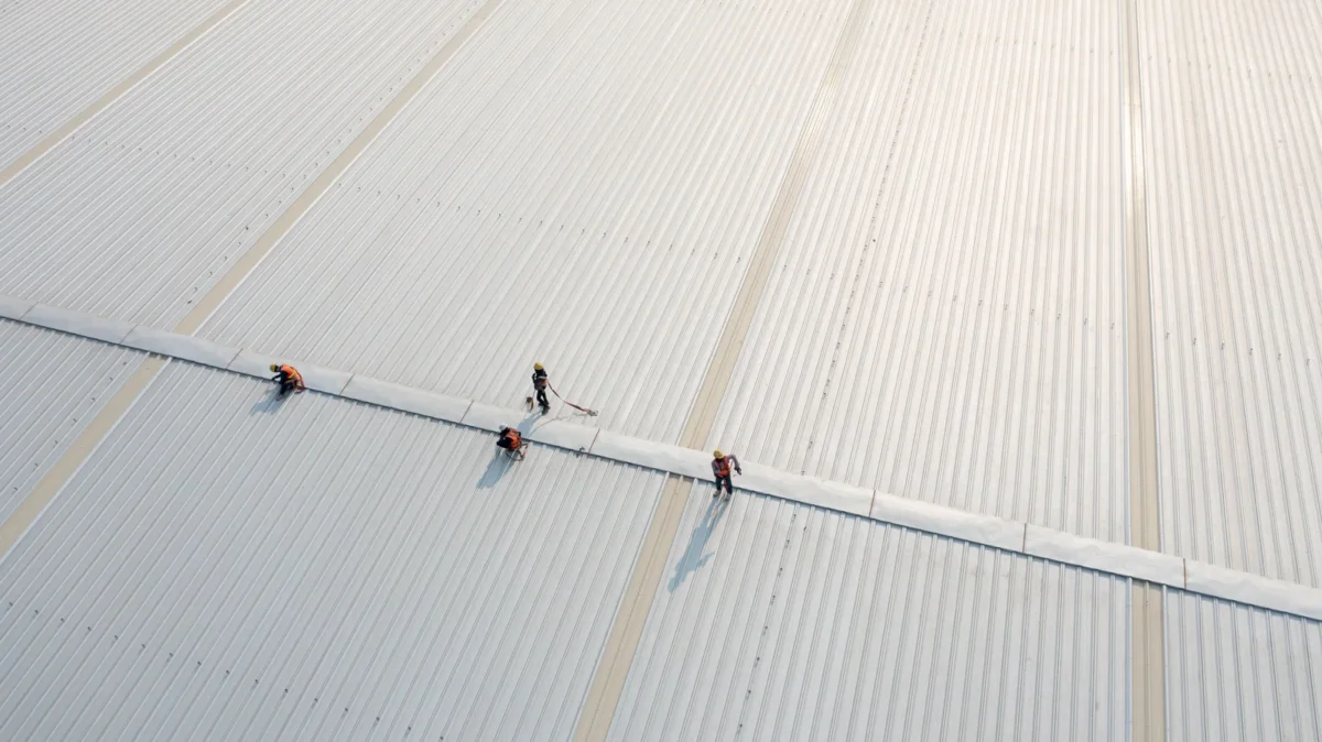 Workers carrying out maintenance on a large ribbed metal industrial roof