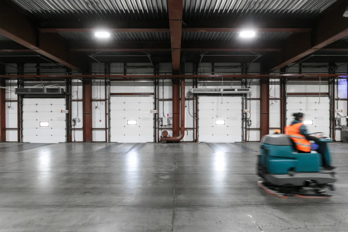 Operator driving a floor cleaning machine through a warehouse